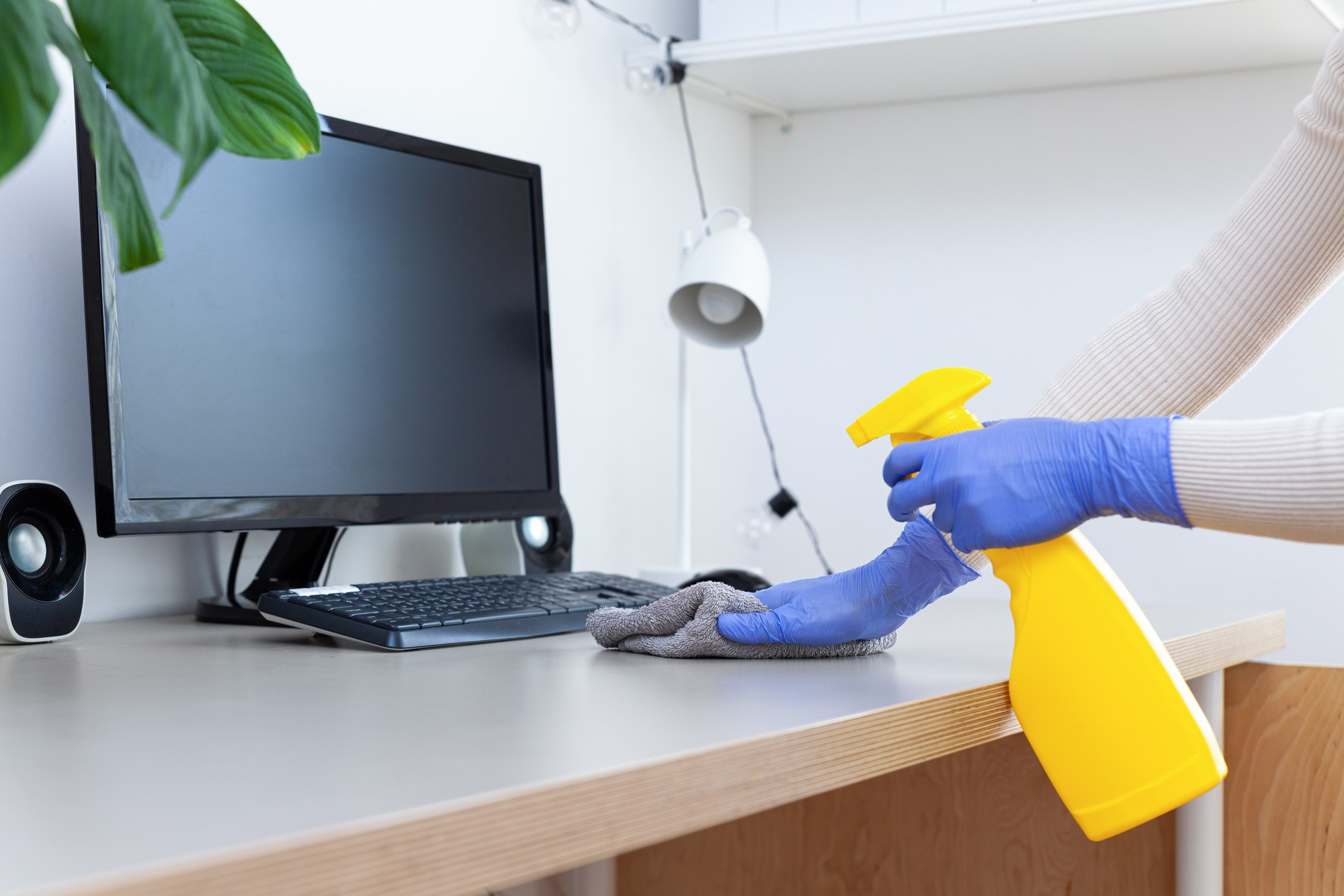 Reinigungskraft wischt Schreibtisch Reinigungskraft wischt Schreibtisch vor Monitor mit Sprühflasche